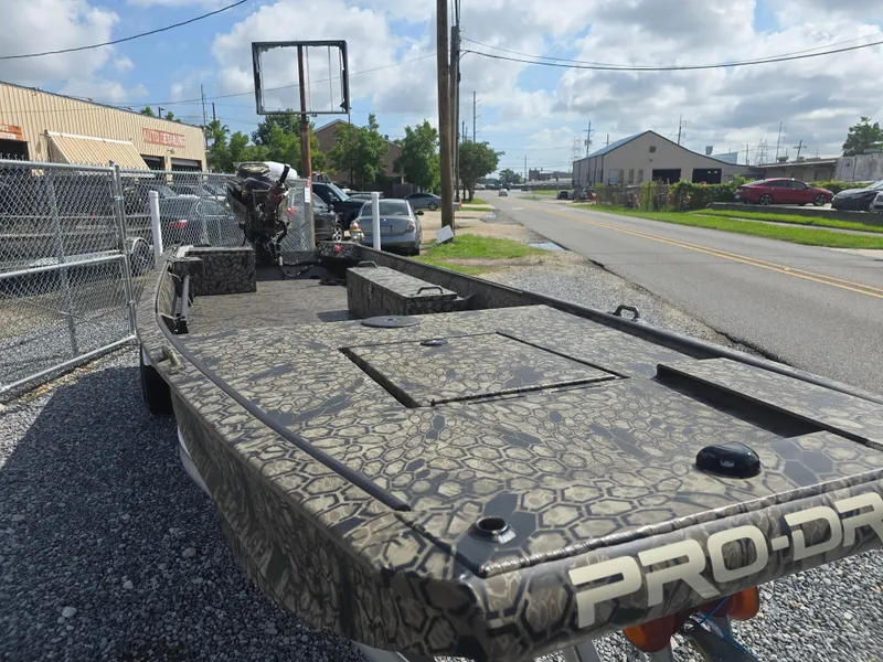 Slide: The Image of 2025 Pro-Drive 1848 SBX boat with camouflage design parked on gravel near a fence. - 9