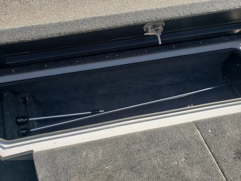 Slide: The Image of 2023 Avid 18XB boat storage compartment with carpeted interior and metal rod. - 18