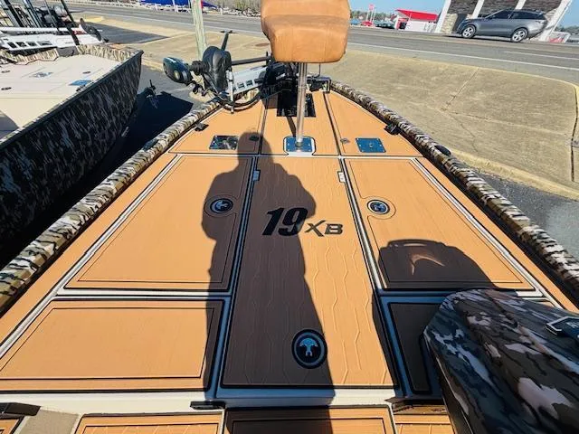 Slide: The Image of 2024 Avid 19XB boat deck with tan finish and camouflage accents, parked outdoors. - 11