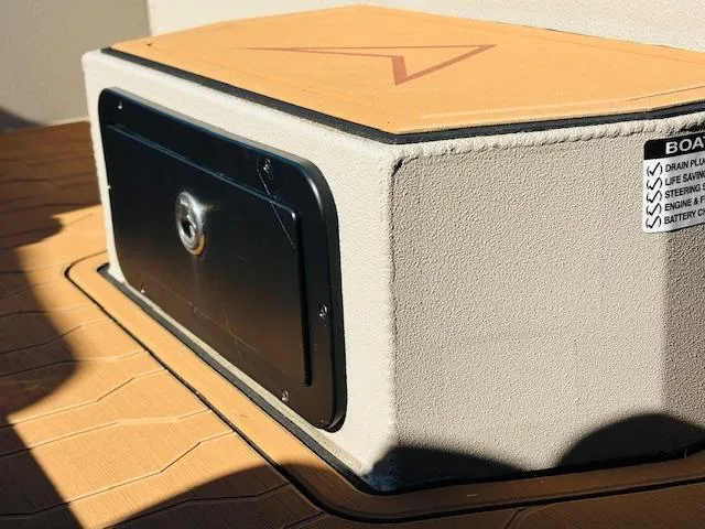 Slide: The Image of 2024 Avid 19XB boat storage compartment with lock, featuring beige and black design. - 13