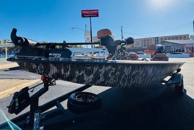 Slide: The Image of 2024 Avid 19XB boat on trailer, camo design, parked outdoors under clear sky. - 2