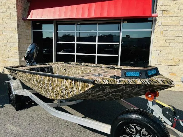 Slide: The Image of Avid 16COM 2025 camouflage boat on trailer outside a building. - 1