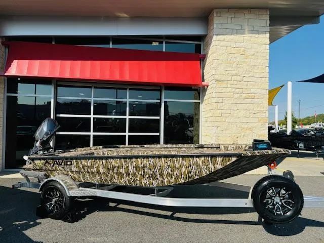 Slide: The Image of 2025 Avid 16COM boat with camouflage design on a trailer, parked outside a building. - 15