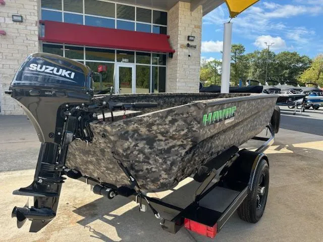 Slide: The Image of 2024 Havoc Boats 1550 VJ with Suzuki motor, camo design, on trailer outside dealership. - 11