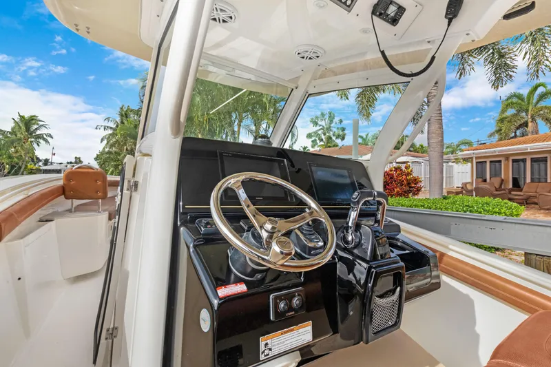 Slide: The Image of 2018 Scout 320 LXF boat helm with steering wheel and controls, docked near palm trees. - 13
