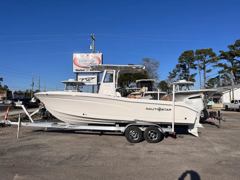 The Image of 2025 NauticStar 242L Offshore boat on trailer, parked outdoors under clear blue sky. - 0