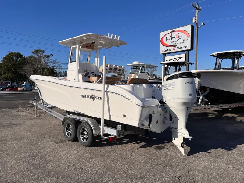 Slide: The Image of 2025 NauticStar 242L Offshore boat on trailer at dealership, featuring Suzuki outboard motor. - 2