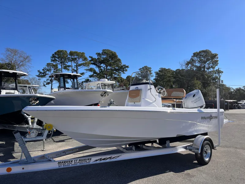 Slide: The Image of 2025 NauticStar 194 Bay boat on trailer, parked outdoors under clear blue sky. - 1
