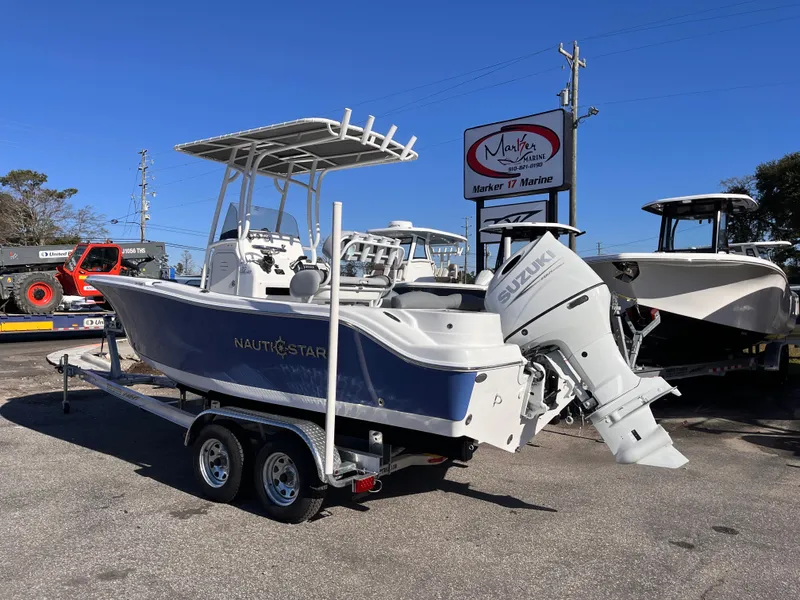 Slide: The Image of 2025 NauticStar 212 Legacy boat on trailer, displayed outdoors at a marine dealership. - 2