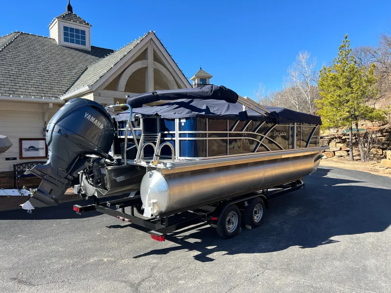 Slide: The Image of 2025 Sylvan Mirage Fish 8522 Party Fish pontoon boat on trailer, parked near a house. - 12