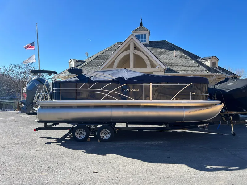 Slide: The Image of 2025 Sylvan Mirage Fish 8522 Party Fish pontoon boat on trailer, parked outdoors. - 13