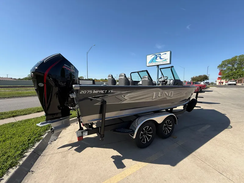 Slide: The Image of 2025 Lund 2075 IMPACT XS boat on trailer, parked outdoors under clear blue sky. - 2
