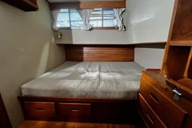 Slide: The Image of 1984 Grand Banks Trawler cabin with wooden interior, bed, drawers, and curtained window. - 11