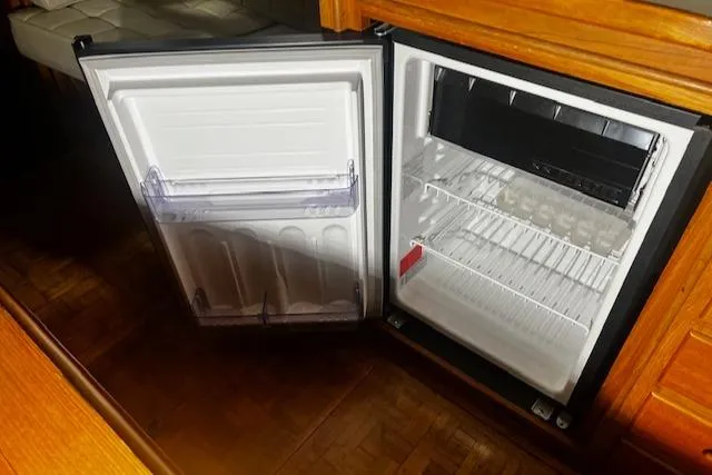 Slide: The Image of Open refrigerator inside 1984 Grand Banks Trawler, showcasing empty shelves and wooden interior. - 16