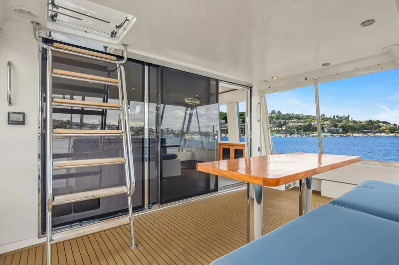 Slide: The Image of 2003 Pacific Mariner Pilothouse yacht interior with wooden table, seating, and ladder, overlooking water. - 3