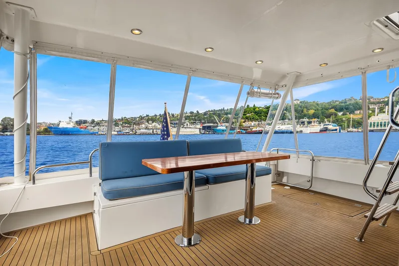 Slide: The Image of 2003 Pacific Mariner Pilothouse yacht interior with blue seating and wooden table, overlooking marina. - 4