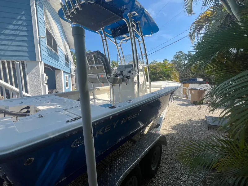 Slide: The Image of 2021 Key West 210 Bay Reef boat on trailer, parked outdoors near a blue house. - 2