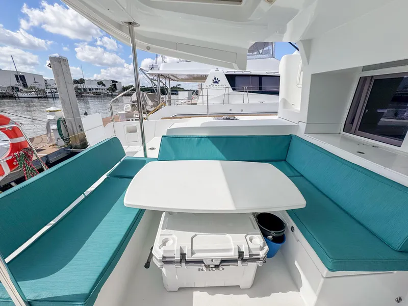 Slide: The Image of Outdoor seating area on a 2017 Lagoon 450 F catamaran, featuring turquoise cushions and a white table. - 7