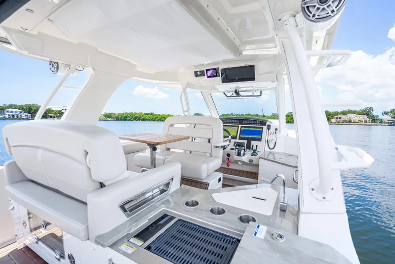 Slide: The Image of 2021 Boston Whaler 350 Realm interior with seating, helm, and kitchenette on a sunny day. - 29