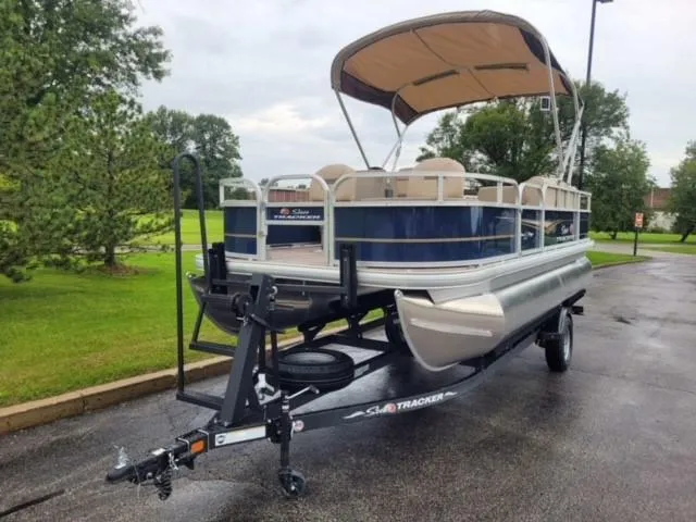 Slide: The Image of 2025 Sun Tracker Bass Buggy 18 DLX pontoon boat on trailer, parked outdoors. - 31