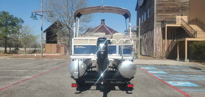 Slide: The Image of 2025 Sun Tracker Bass Buggy 16 XL Select pontoon boat parked in a lot. - 2