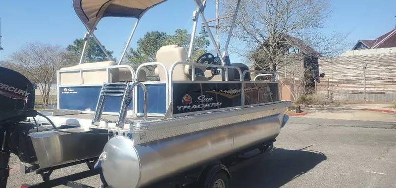 Slide: The Image of 2025 Sun Tracker Bass Buggy 16 XL Select pontoon boat on trailer, parked outdoors. - 3