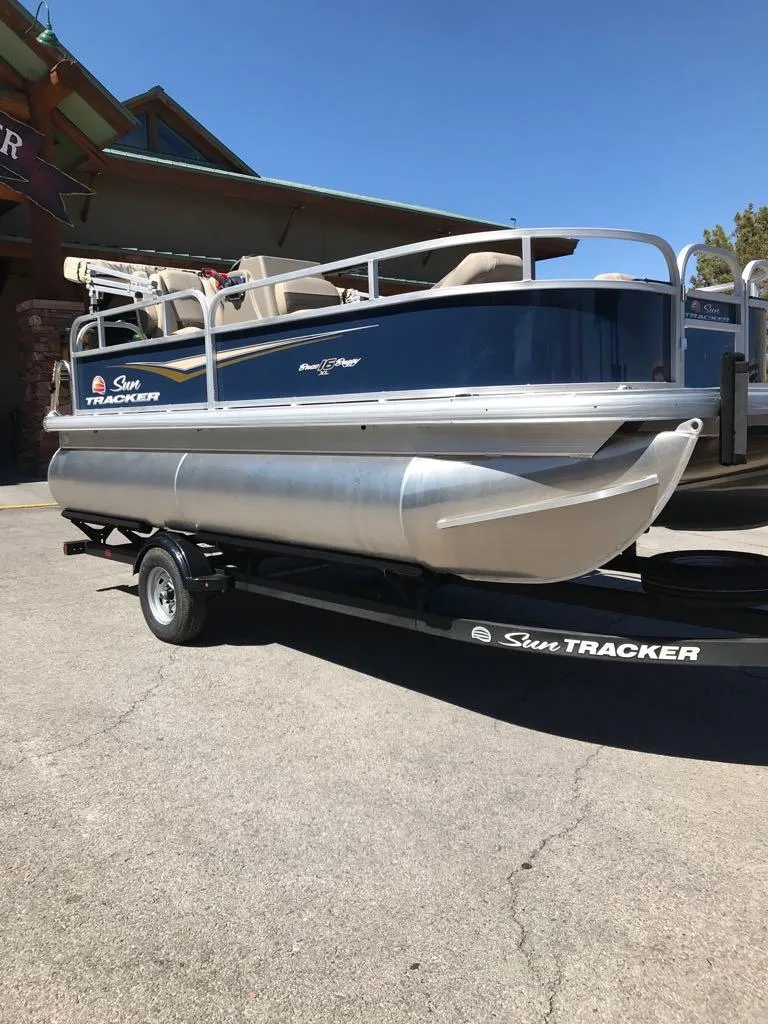 Slide: The Image of 2025 Sun Tracker Bass Buggy 16 XL Select pontoon boat on trailer, parked outdoors. - 5