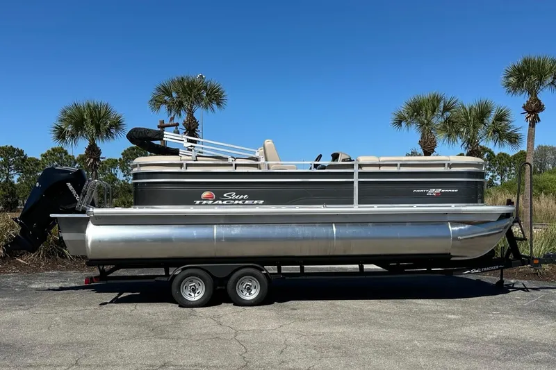 The Image of 2025 Sun Tracker Party Barge 22 XP3 pontoon boat on trailer, parked outdoors. - 0