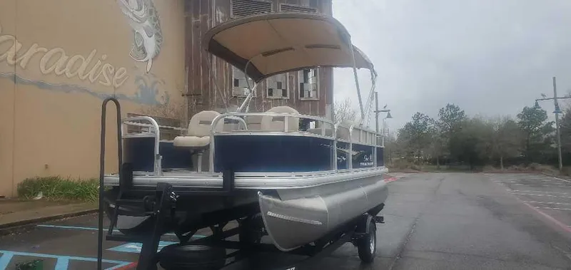 Slide: The Image of 2025 Sun Tracker Bass Buggy 18 DLX pontoon boat on trailer, parked outdoors. - 2
