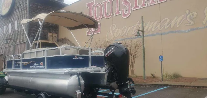 Slide: The Image of 2025 Sun Tracker Bass Buggy 18 DLX pontoon boat parked outside a store. - 3