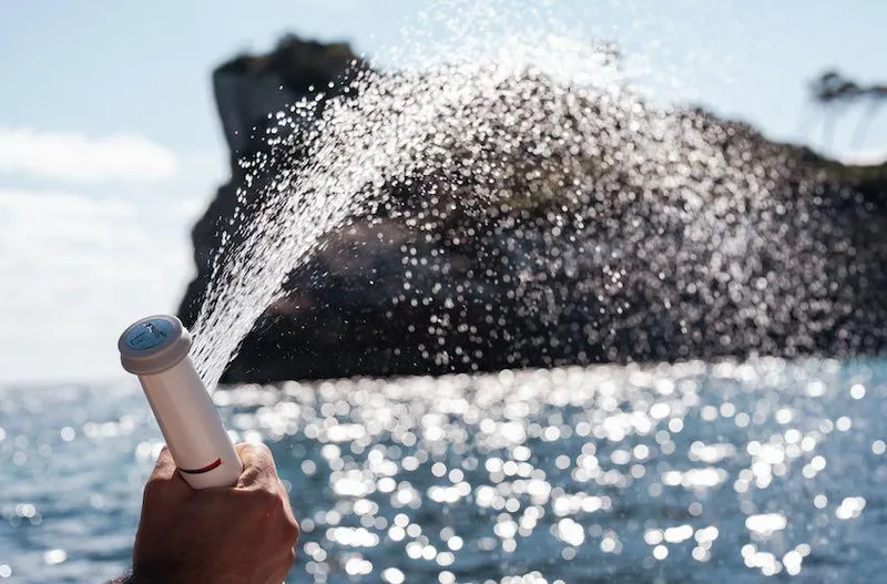 Slide: The Image of Hand spraying water from Navan S30 device, ocean and rocky island in background, 2025. - 12