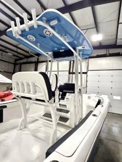 Slide: The Image of 2025 Tidewater 198 CC Adventure boat in a warehouse, featuring a blue T-top and white seating. - 8