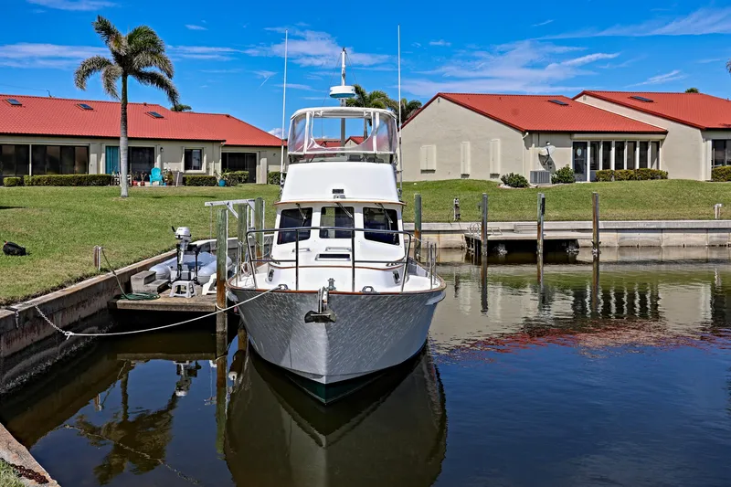 Slide: The Image of Legacy Flybridge Downeast 2000 boat docked near waterfront homes with red roofs and palm trees. - 0