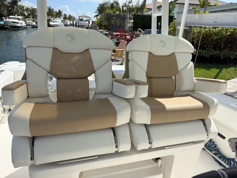 Slide: The Image of 2019 Edgewater 320CC boat seats with beige and white upholstery, docked near a canal. - 28
