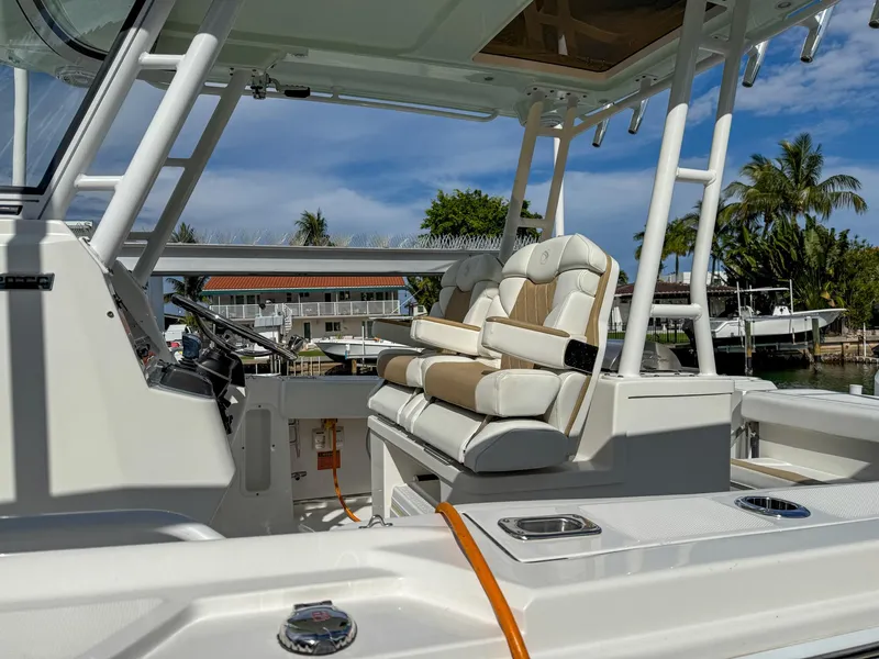 Slide: The Image of 2019 Edgewater 320CC boat interior with cushioned seating and helm, docked near palm trees. - 34