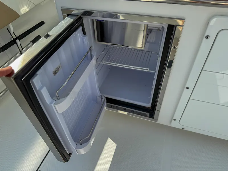 Slide: The Image of Open mini fridge on 2019 Edgewater 320CC boat, showcasing interior storage space. - 53
