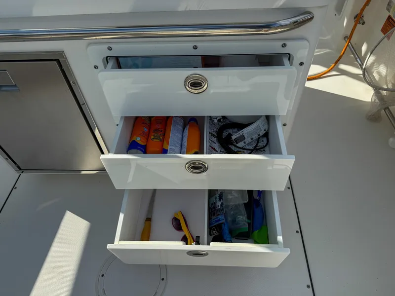 Slide: The Image of Open storage drawers on a 2019 Edgewater 320CC boat, containing various items. - 54