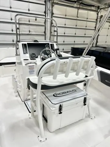 Slide: The Image of 2024 Robalo R180 boat interior with helm, rod holders, and branded cooler in a garage setting. - 8