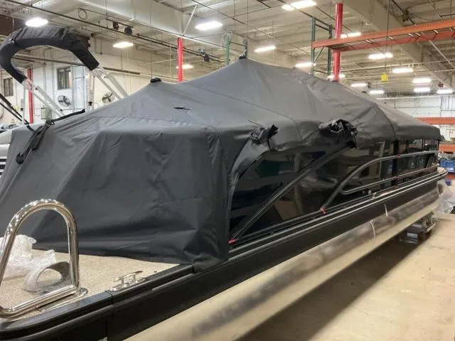 Slide: The Image of 2025 Bennington M Quad Bench 26 MFB pontoon boat covered in a black tarp in a warehouse. - 15
