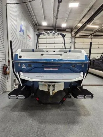 Slide: The Image of 2024 Axis Wake Research A245 boat in a showroom, rear view with blue and white design. - 4