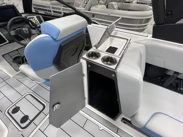 Slide: The Image of 2024 Malibu 24 MXZ boat interior with blue and white seating, open storage, and cup holders. - 10