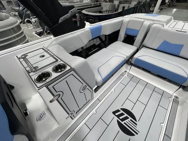 Slide: The Image of 2024 Malibu 24 MXZ boat interior with gray and blue seating, cup holders, and logo on floor. - 9