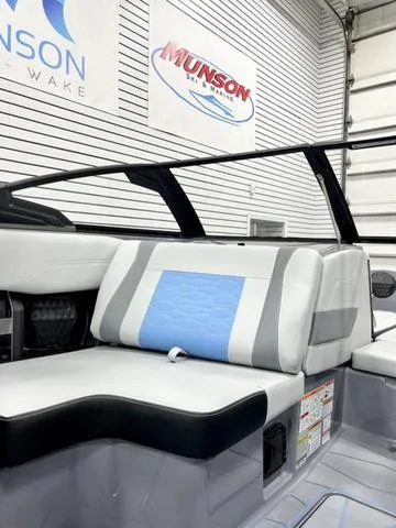 Slide: The Image of 2024 Malibu 23 MXZ boat interior with blue and gray seating in showroom. - 14