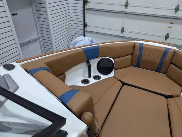Slide: The Image of 2025 Malibu 23 LSV boat interior with tan and blue seating in a garage. - 7
