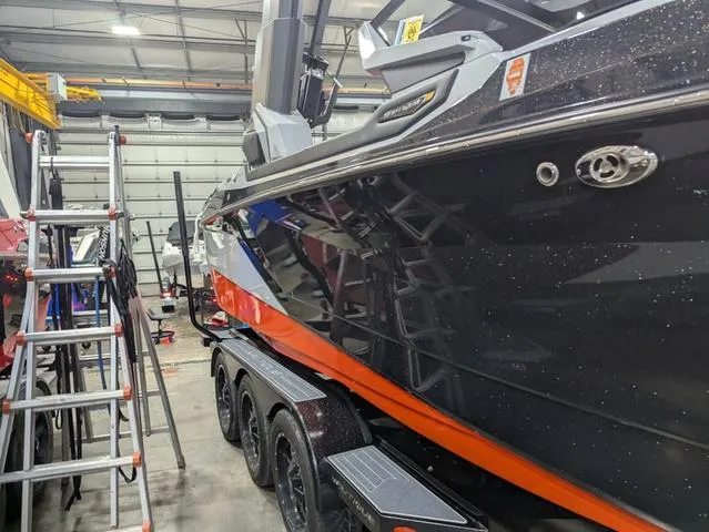 Slide: The Image of 2020 Nautique G23 Paragon boat in a garage, black and orange exterior, triple-axle trailer. - 5