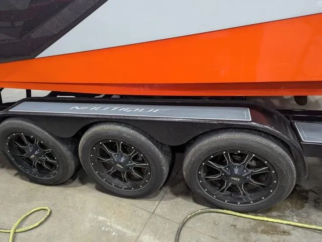 Slide: The Image of 2020 Nautique G23 Paragon boat trailer with black wheels and orange hull. - 9
