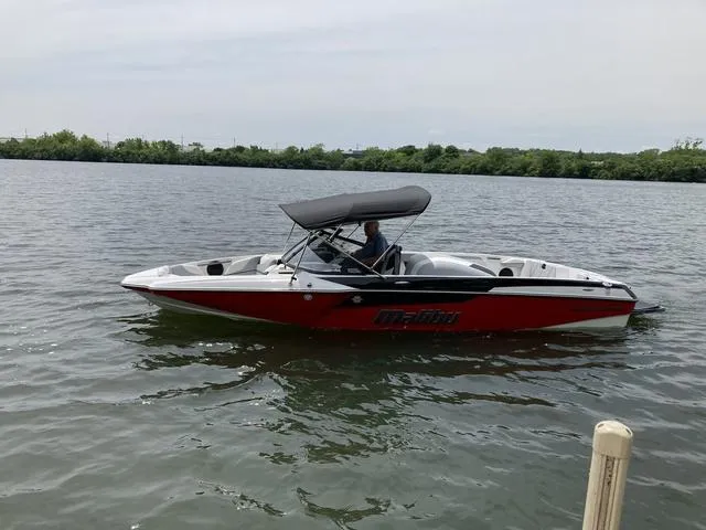 Slide: The Image of 2024 Malibu TXi Mo boat on a calm lake with a canopy. - 11
