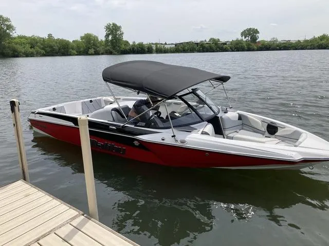 Slide: The Image of 2024 Malibu TXi Mo boat with black canopy docked on a calm lake. - 4