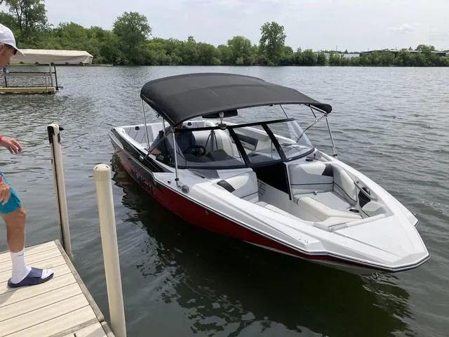 Slide: The Image of 2024 Malibu TXi Mo boat docked on a calm lake with a canopy. - 5