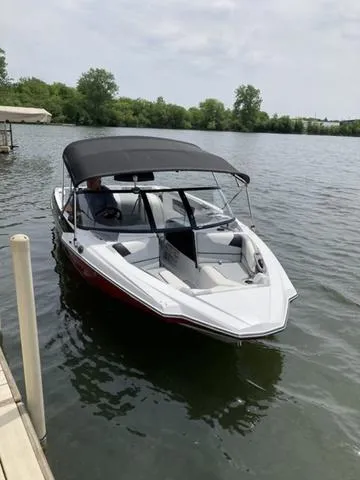Slide: The Image of 2024 Malibu TXi Mo boat docked on a calm lake under a cloudy sky. - 6